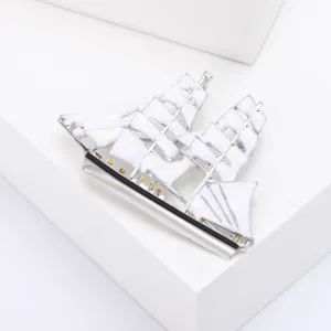 Gedetailleerde macro-opname van een zilveren zeilbootbroche met witte emaille zeilen