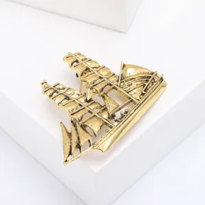 Close-up van een vintage gouden zeilboot broche met gedetailleerde zeilen op wit.