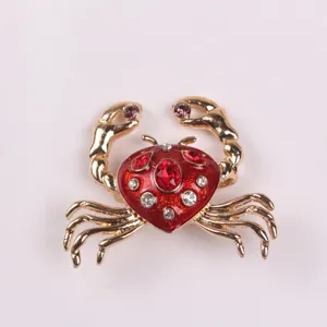 Close-up detail of a gold-tone crab brooch with vibrant red enamel and set with crystals