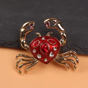 Detailed view of a gold-toned crab brooch with red enamel and sparkling rhinestones.