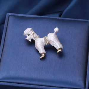 Détail d'une broche caniche en émail blanc avec strass sur un fond en soie bleue.