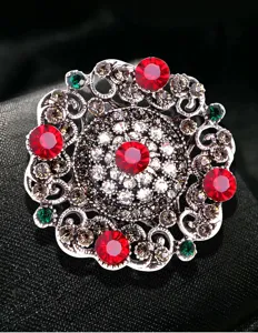 Macro view of vintage Baroque palace style brooch featuring red and green crystals on metal