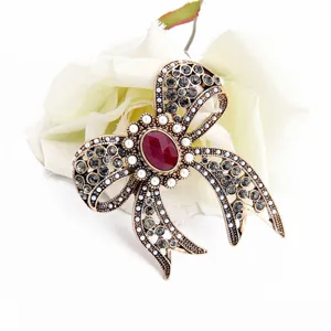 Detail of vintage bow brooch with red gemstone, rhinestones, and pearls on white rose