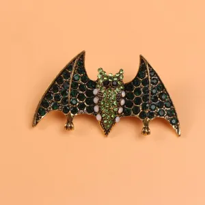 Close-up detail of a vintage style bat brooch adorned with green rhinestones and gold alloy