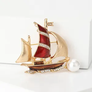 Detailed view of a gold sailboat brooch with red enamel sails and pearl accent
