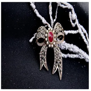 Macro view of a vintage bow brooch with a central red gemstone and decorative pearls.
