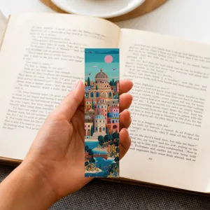 Hand holding a colorful retro city illustration paper bookmark over an open book
