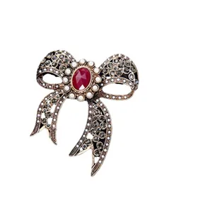 Elegant vintage bow brooch for women with red gemstone center and grey rhinestones