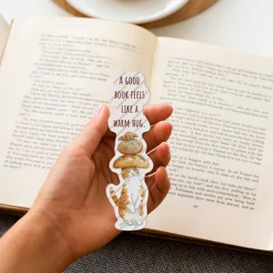 Hand holding a cute cartoon cat bookmark with warm English quote over an open book
