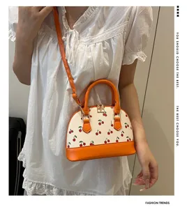 Detailaufnahme einer cremefarbenen Muscheltasche mit Kirschprint und orangefarbenem Leder.