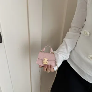 Close-up of a luxury mini pink crossbody bag with gold chain strap being held by hand