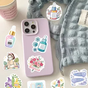 Close-up of various cartoon skincare stickers on a lavender phone case and light blue fabric.