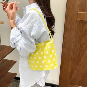 Detail van een gele polka dot schoudertas gedragen door een model in een lifestyle setting.