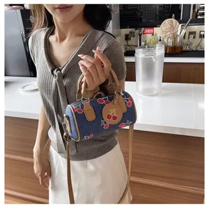 Detailed view of a small denim Boston bag with cherry embroidery held by a model in a cafe