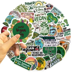 Une main tient un autocollant World Vegan Day devant un grand lot de 50 stickers