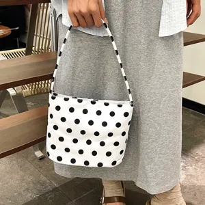 Detailweergave van een stijlvolle witte handtas met stippen vastgehouden door een model.
