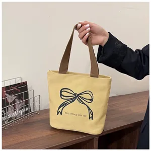 Bolso de lona amarillo con estampado de lazo y asas marrones sobre madera