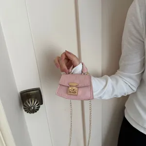 Close-up of a miniature pink textured crossbody bag held by hand with elegant gold hardware.