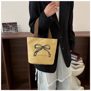 Bolso tote de lona amarilla con estampado de lazo negro llevado por una modelo
