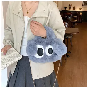 Vista detallada de un bolso de peluche gris con ojos grandes y cadena de metal dorada