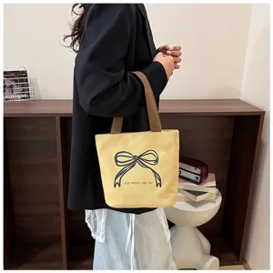 Bolso tote de lona amarilla con estampado de lazo sostenido por modelo en blazer negro