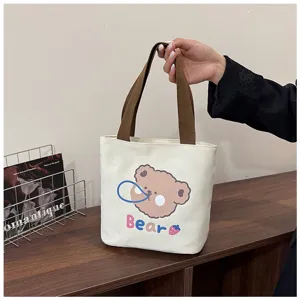 Detalle de un bolso tote de lona crema con estampado de un lindo oso y asas marrones.