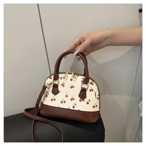 Detailansicht einer weißen Muschel-Handtasche mit Kirschmuster und braunem Leder.