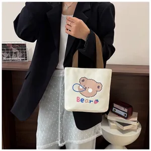 Primer plano de un bolso tote de lona crema con estampado de un lindo oso llevado por una modelo