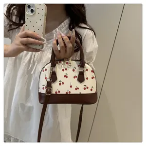 Modische Muschel-Handtasche mit Kirschdruck und braunen Trägern in Lifestyle-Umgebung