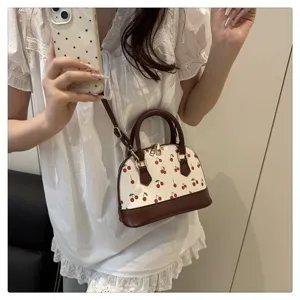 Charmante Mini-Muscheltasche mit Kirschdruck, von Model getragen, Outfit-Detail.