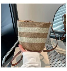 Detalle de un bolso cubo de paja trenzada a mano a rayas con correa de cuero marrón
