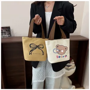 Dos bolsos tote de lona con estampados de lazo y oso sostenidos por una modelo en sala
