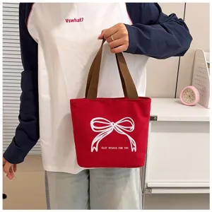 Primer plano de un bolso tote de lona roja con bordado de lazo blanco y asas café.
