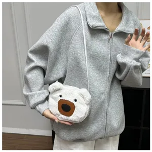 Close-up of a white plush bear-shaped crossbody bag worn with a casual grey hoodie.