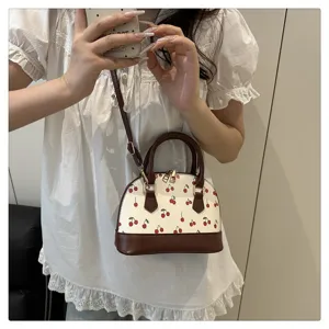 Lifestyle-Foto einer schicken Kirschprint-Muscheltasche mit braunem, verstellbarem Tragegurt.
