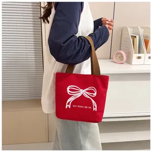 Vista detallada de un bolso de lona rojo con un diseño de lazo blanco y asas cómodas.