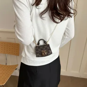 Mini dark brown crossbody charm bag with M monogram pattern shown on model's back view