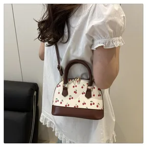 Nahaufnahme einer stylischen weißen Muscheltasche mit Kirschmuster, getragen von einem Model