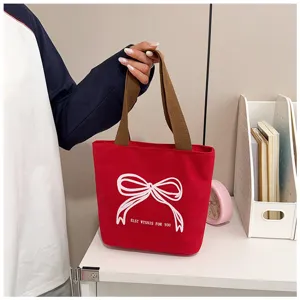 Detalle de bolso tote de lona roja con un elegante diseño de lazo blanco bordado.