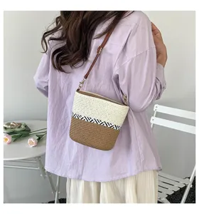 Detalle de un bolso cubo de paja trenzado a mano con bloques de color llevado por una persona.