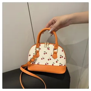 Detailansicht einer orangefarbenen Kuppelhandtasche mit süßen Kirschdrucken und Goldteilen