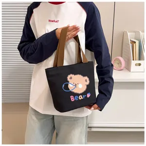 Detalle de un bolso tote de lona negra con un lindo diseño de osito animado, de mano.