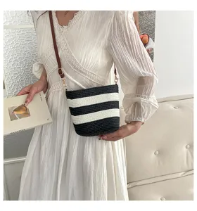 Vista detallada de un bolso de paja a rayas en una modelo con un elegante vestido.