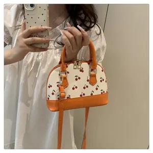 Nahaufnahme einer stylischen weißen Muscheltasche mit Kirschmuster und orangefarbenem Rand.