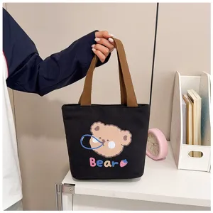 Bolso tote de lona negra con lindo estampado de oso sostenido a mano en un entorno moderno