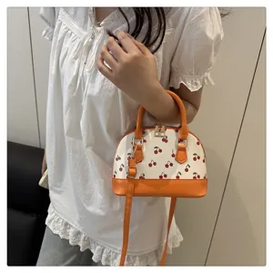 Elegante orangefarbene Muschel-Handtasche mit Kirschdruck von einem Modell gehalten