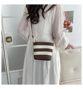 Detalle del bolso de paja tejido a rayas marrones y blancas en modelo con vestido blanco