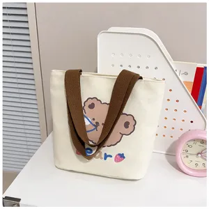 Detalle del bolso tote de lona color crema con un estampado de oso y asas marrones