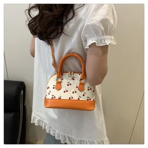 Modell trägt eine süße Kirschdruck-Muscheltasche in Orange und Weiß mit Schultergurt.