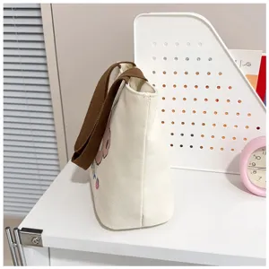 Vista lateral de bolsa de lona blanca con asas marrones y estampado de dibujos animados